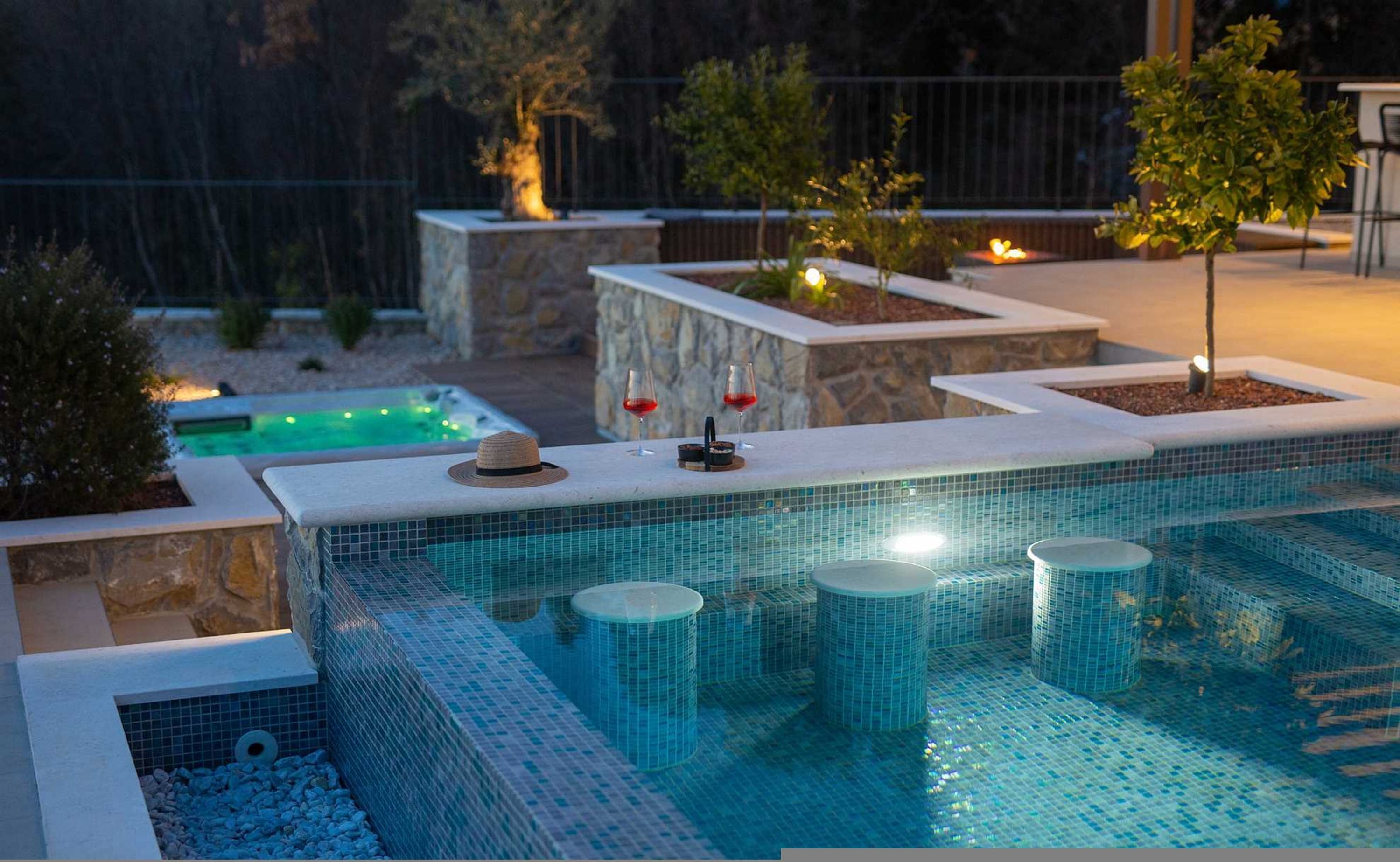 Een zwembad met betegelde rand, een jacuzzi en een loungeruimte met stoelen.