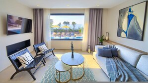 A modern hotel room with a TV, a sofa, a chair, a small table, and a view of a pool. - Villa Lord With Heated Pool Jacuzzi and Sauna (Krk)