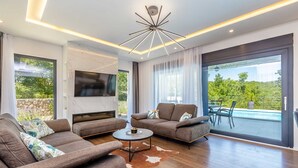 A modern living room with a fireplace, two sofas, a coffee table, and a large TV. - Villa Meraviglia With Private Pool (Krk)