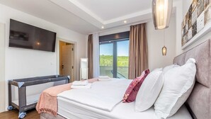 A modern hotel room with a large bed, a flat-screen TV, a balcony with a view, and a ceiling light fixture. - Villa Meraviglia With Private Pool (Krk)