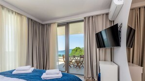 A hotel room with a bed, a TV, and a balcony with a table and chairs. - Villa Vista With Private Pool and Sauna (Krk)