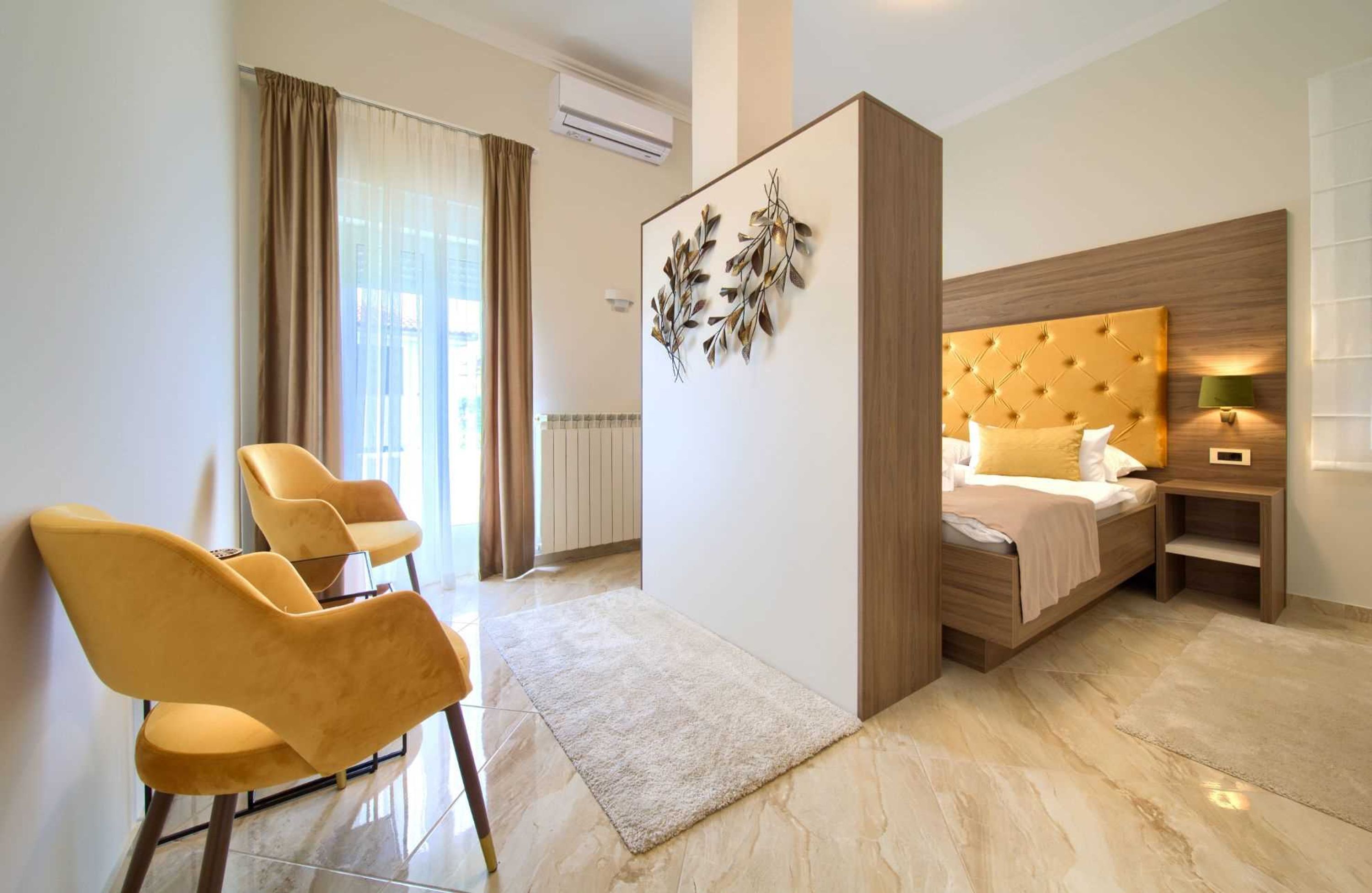 Une chambre d’hôtel moderne comprenant un lit, un coin salon avec deux fauteuils, un élément décoratif mural et une fenêtre avec des rideaux.