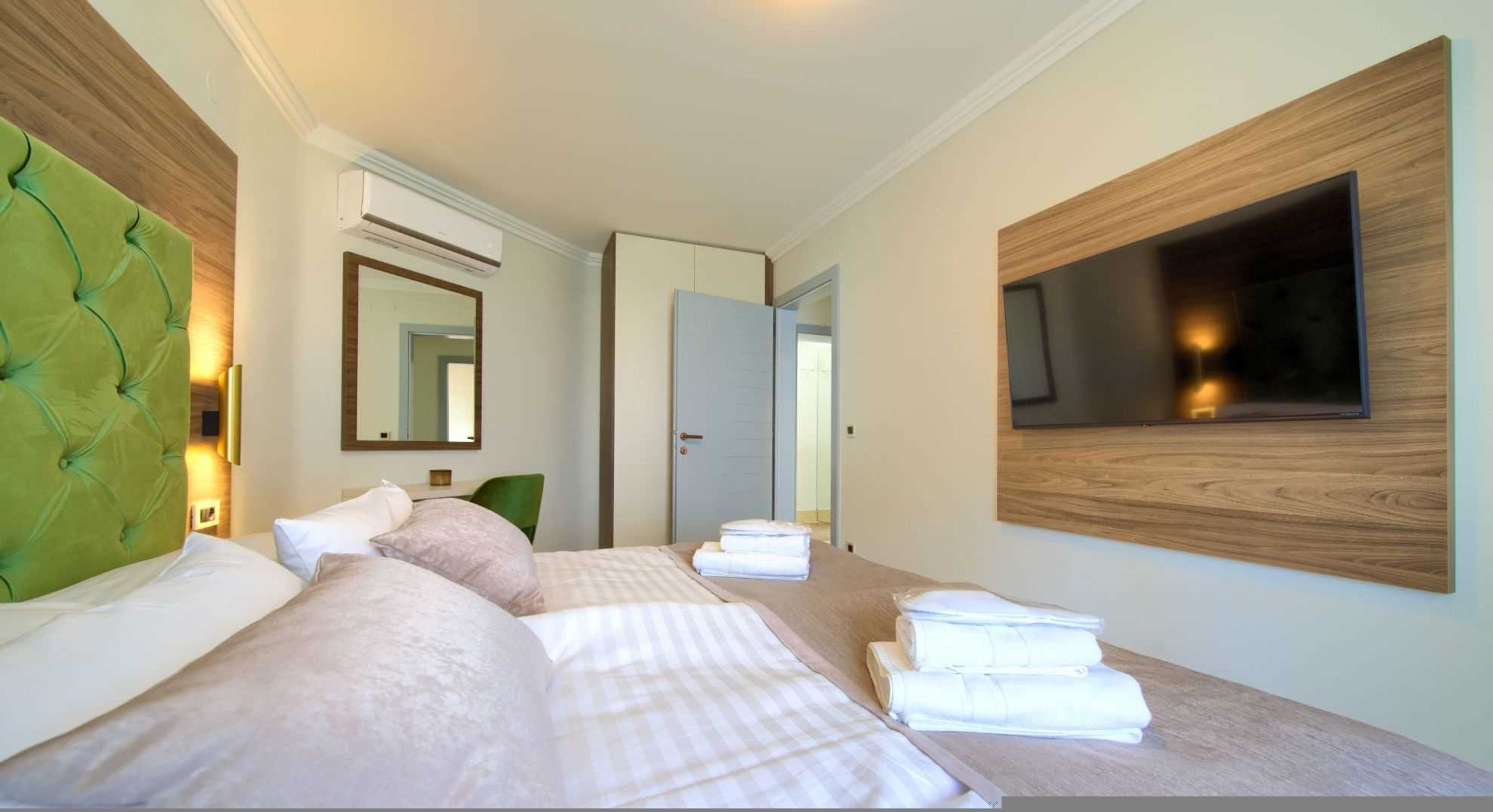 A hotel room with two beds, a large mirror, a flat-screen TV mounted on the wall, and a wooden headboard.
