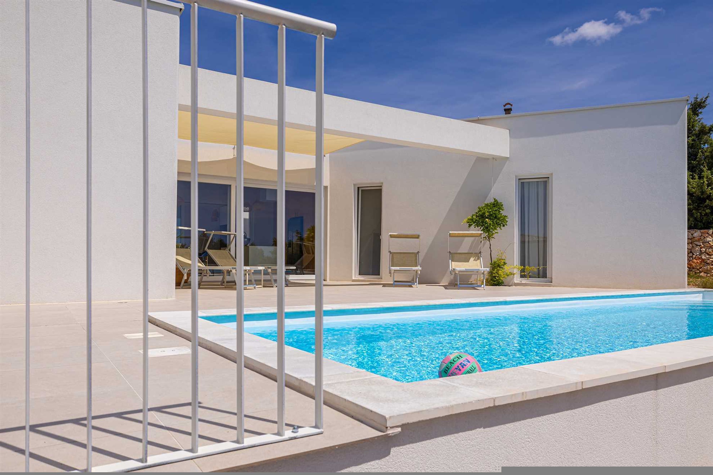 Una casa moderna con piscina, un patio cubierto y un cielo azul despejado.