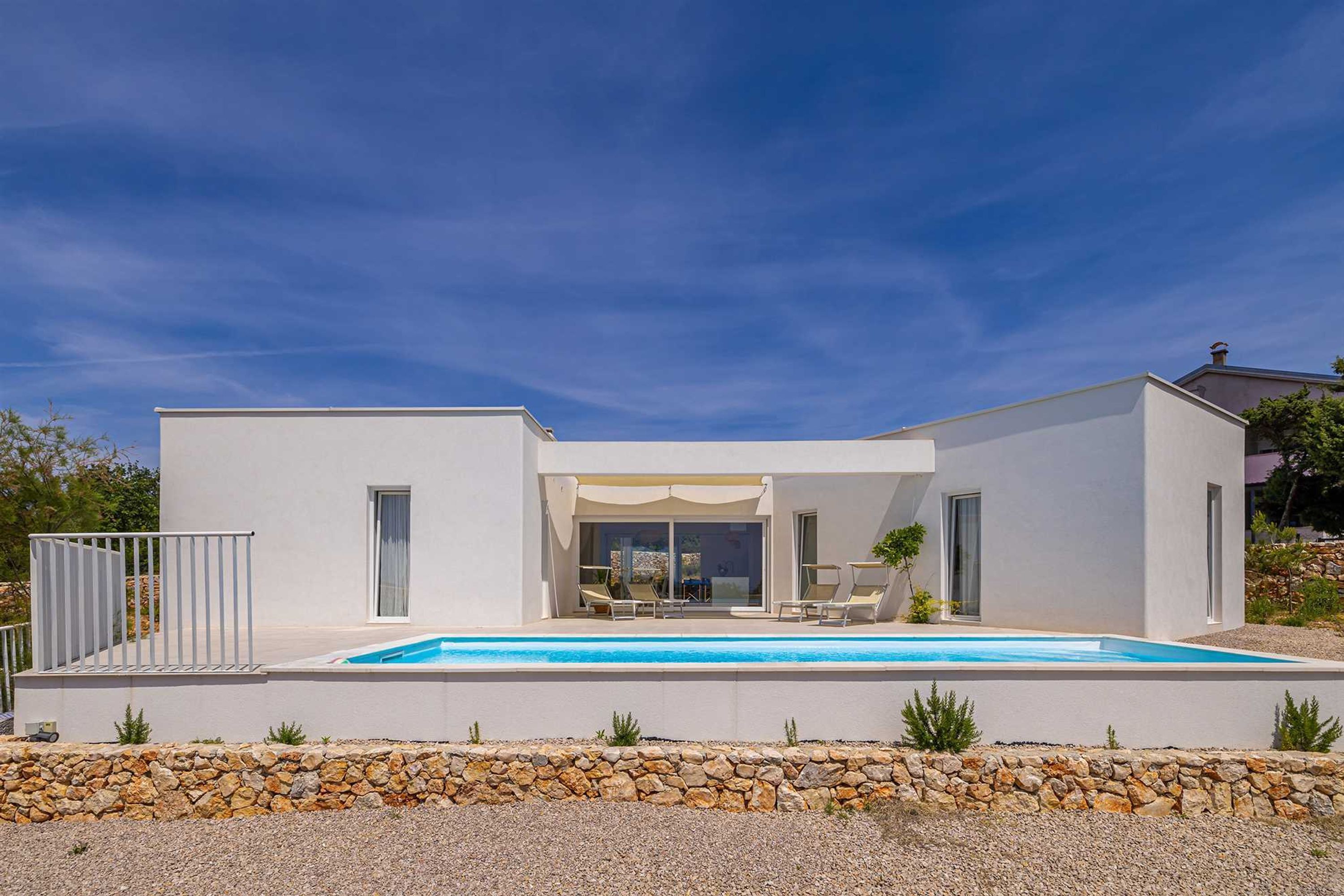 A modern two-story house with a swimming pool, stone retaining wall, and a covered patio area.