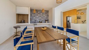 A modern kitchen with a wooden dining table, blue cushioned chairs, and hanging wicker pendant lights. - Villa Menta IV in Linardici (Krk)