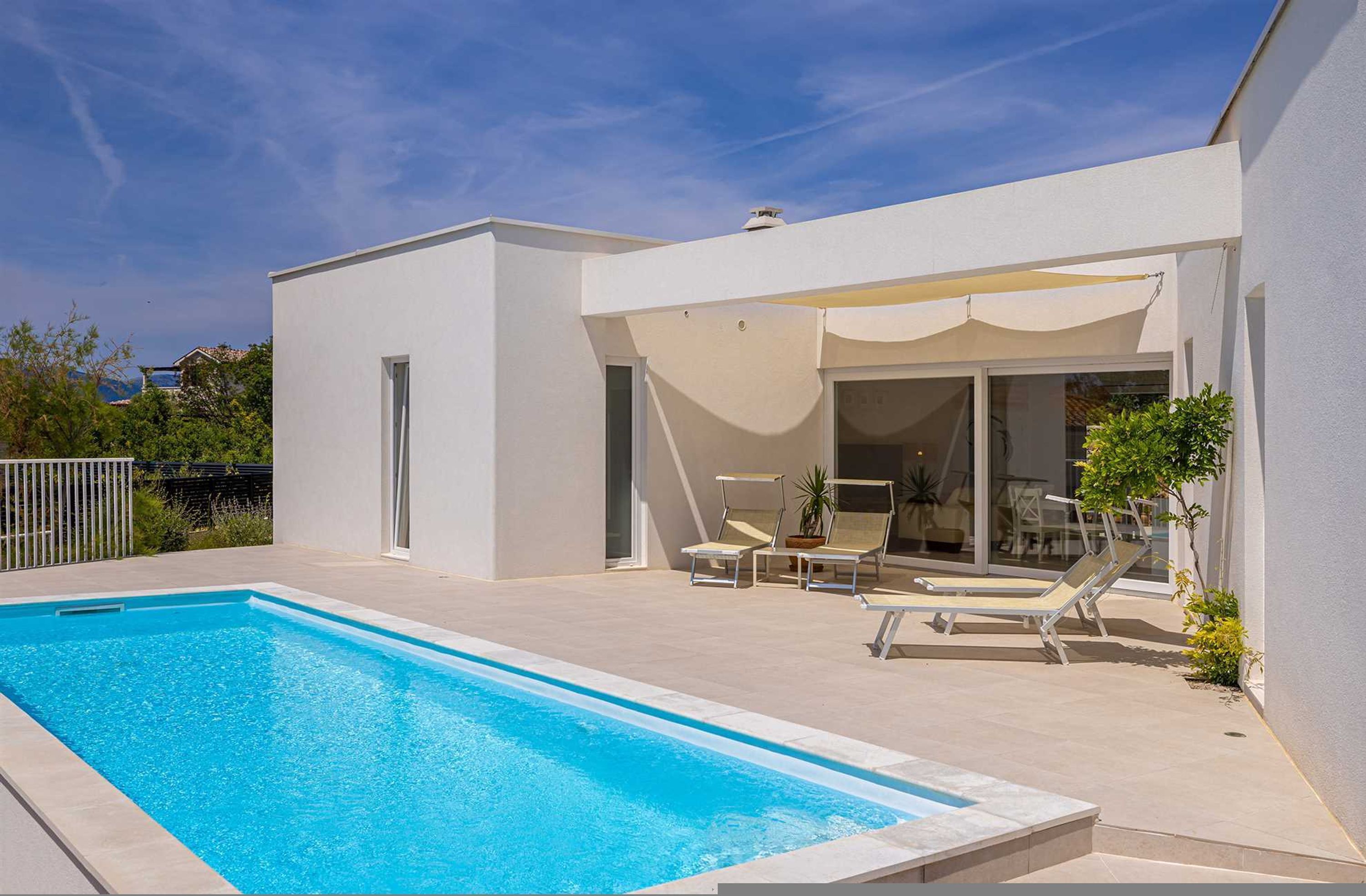 A modern house with a swimming pool, a covered patio with lounge chairs, and a view of the surrounding area.