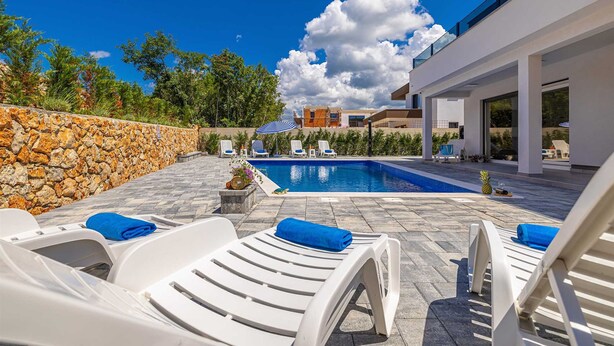 A modern outdoor pool area with white lounge chairs and a stone wall. - Villa Katharina With Private Pool (Krk)