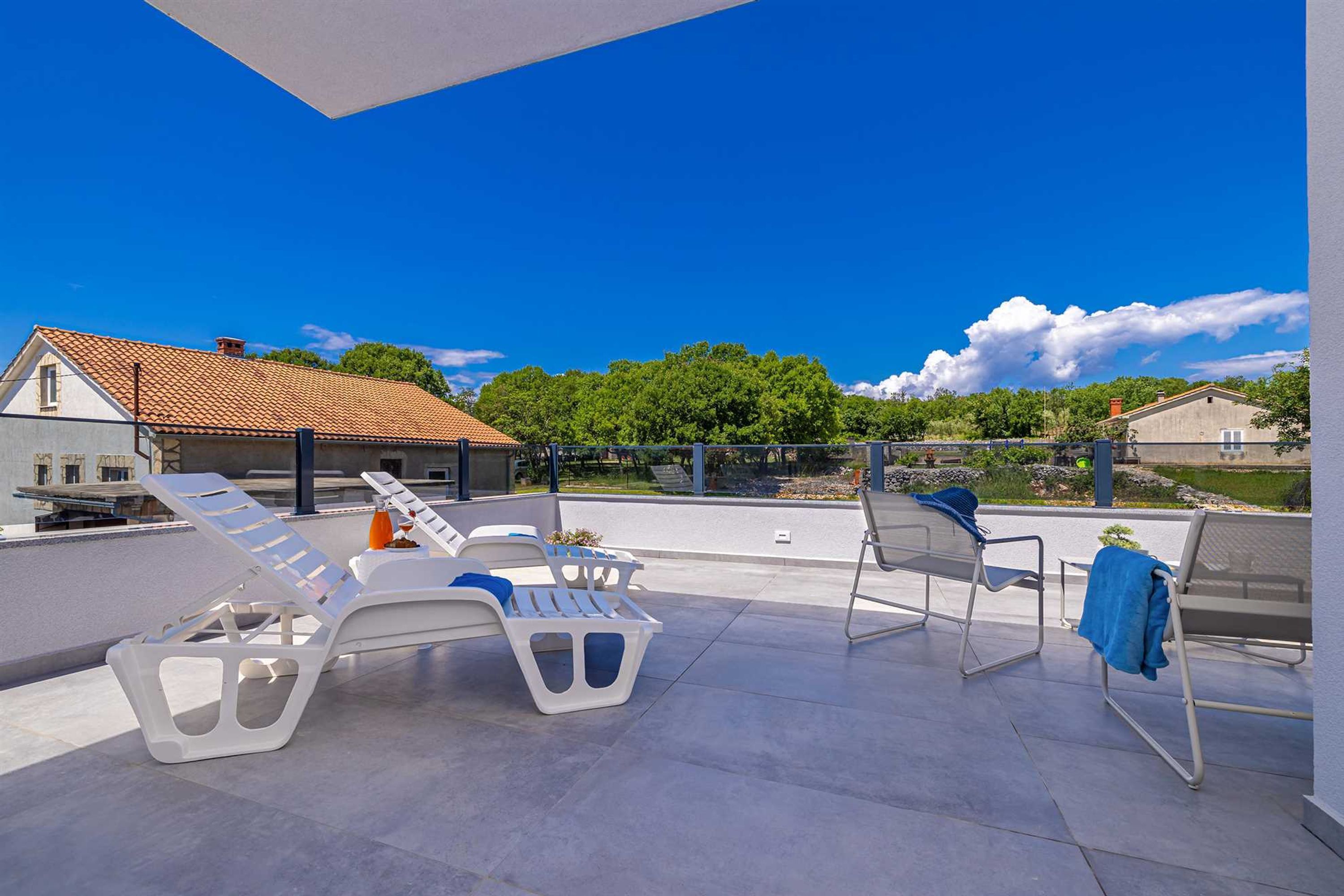 Eine Dachterrasse mit Liegestühlen und einem Tisch mit Blick auf eine Wohngegend mit Bäumen und Häusern.