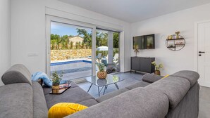 A modern living room with grey sofas, a glass coffee table, and a TV on the wall. - Villa Katharina With Private Pool (Krk)