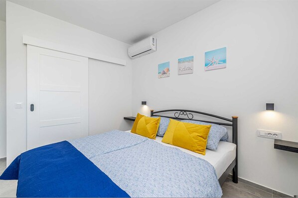 Une chambre à coucher avec un lit, une porte blanche, un climatiseur et des œuvres d’art accrochées au mur.
