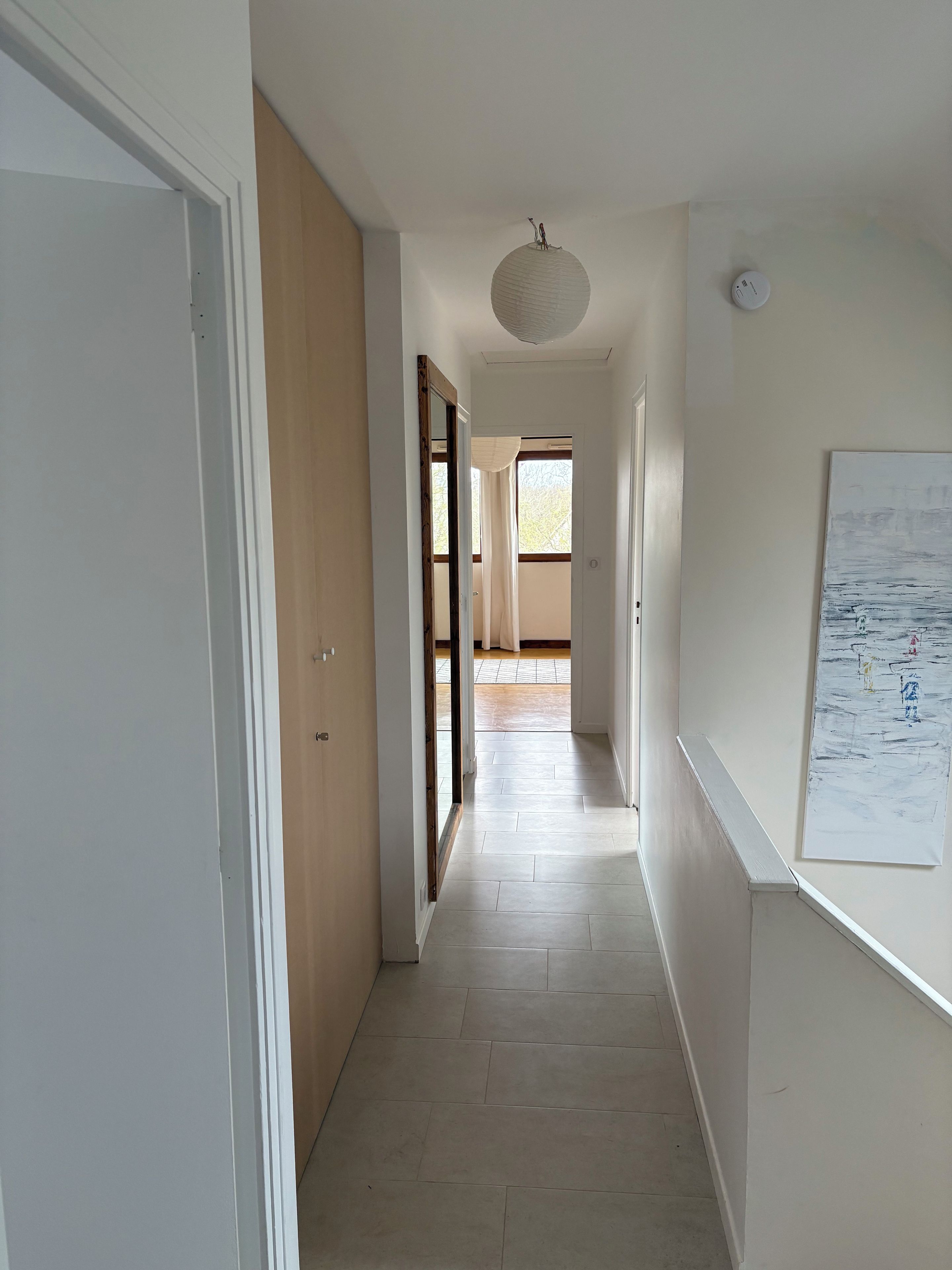 Un couloir avec une porte à gauche, un luminaire au plafond et un mur orné d’une affiche.