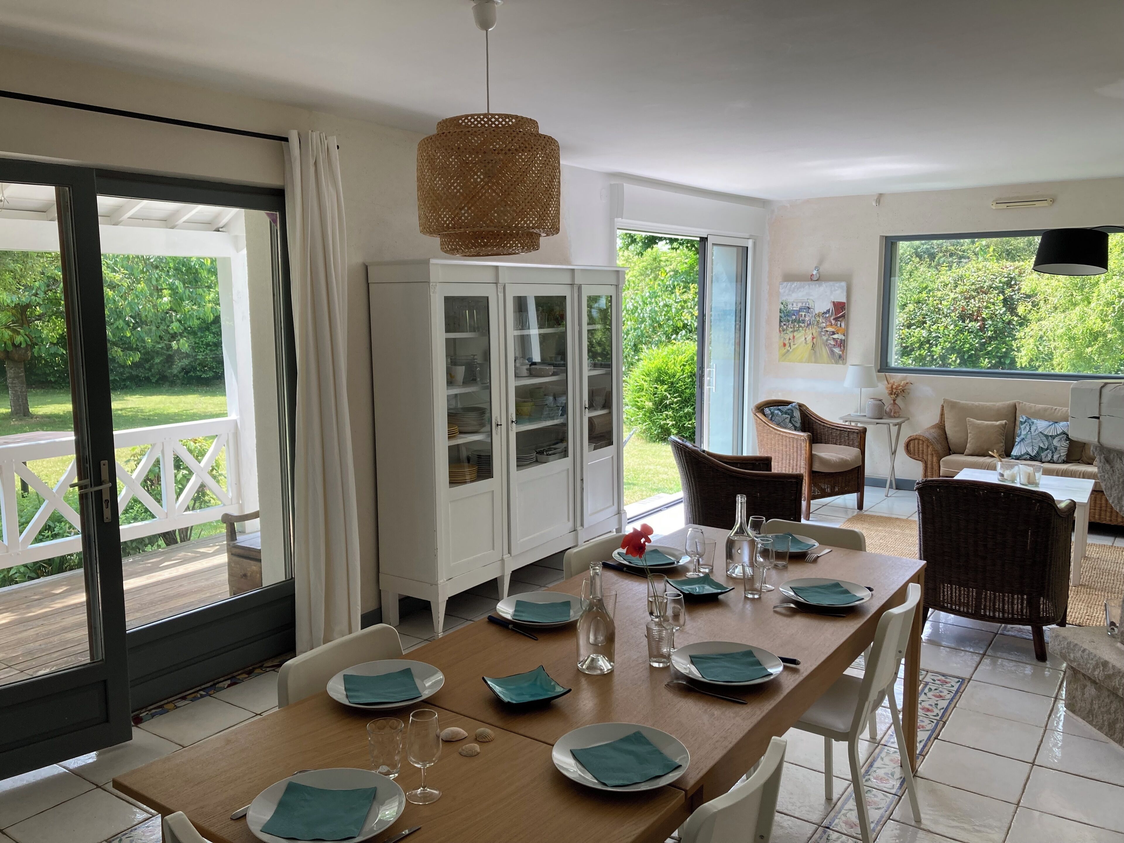 A dining area with a table set for four, a cabinet with glass doors, wicker furniture, and a view of the outdoors.