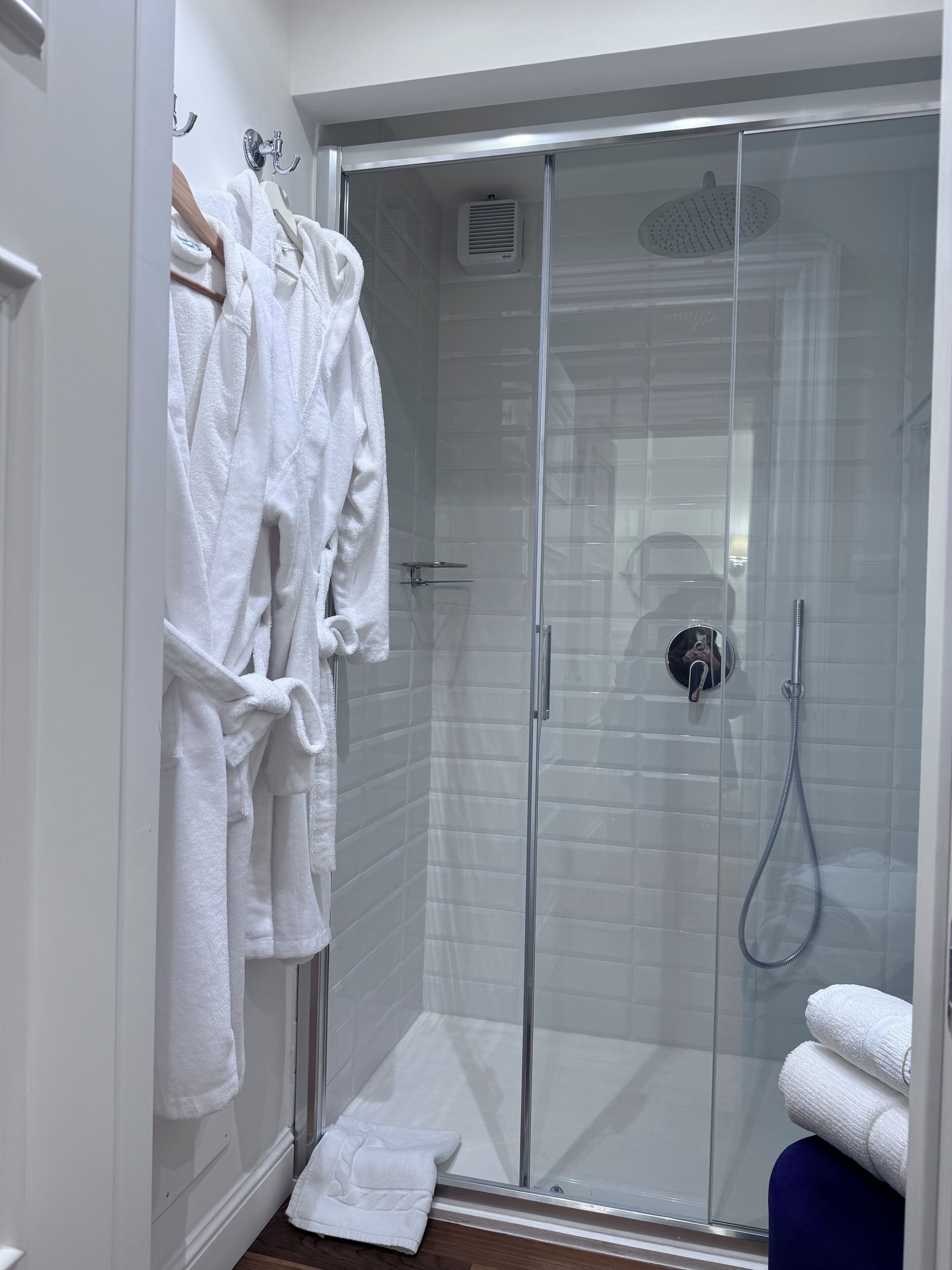 A modern bathroom with a glass-enclosed shower, white towels, and a wooden bath mat.