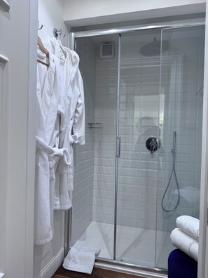 A modern bathroom with a glass-enclosed shower, white towels, and a wooden bath mat.