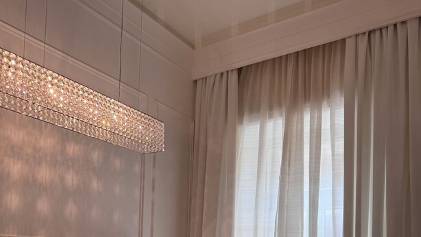 Ein Schlafzimmer mit einer gepolsterten Kopfstütze, einem großen Fenster mit leichtem Vorhang und einem Nachttisch mit Lampe.