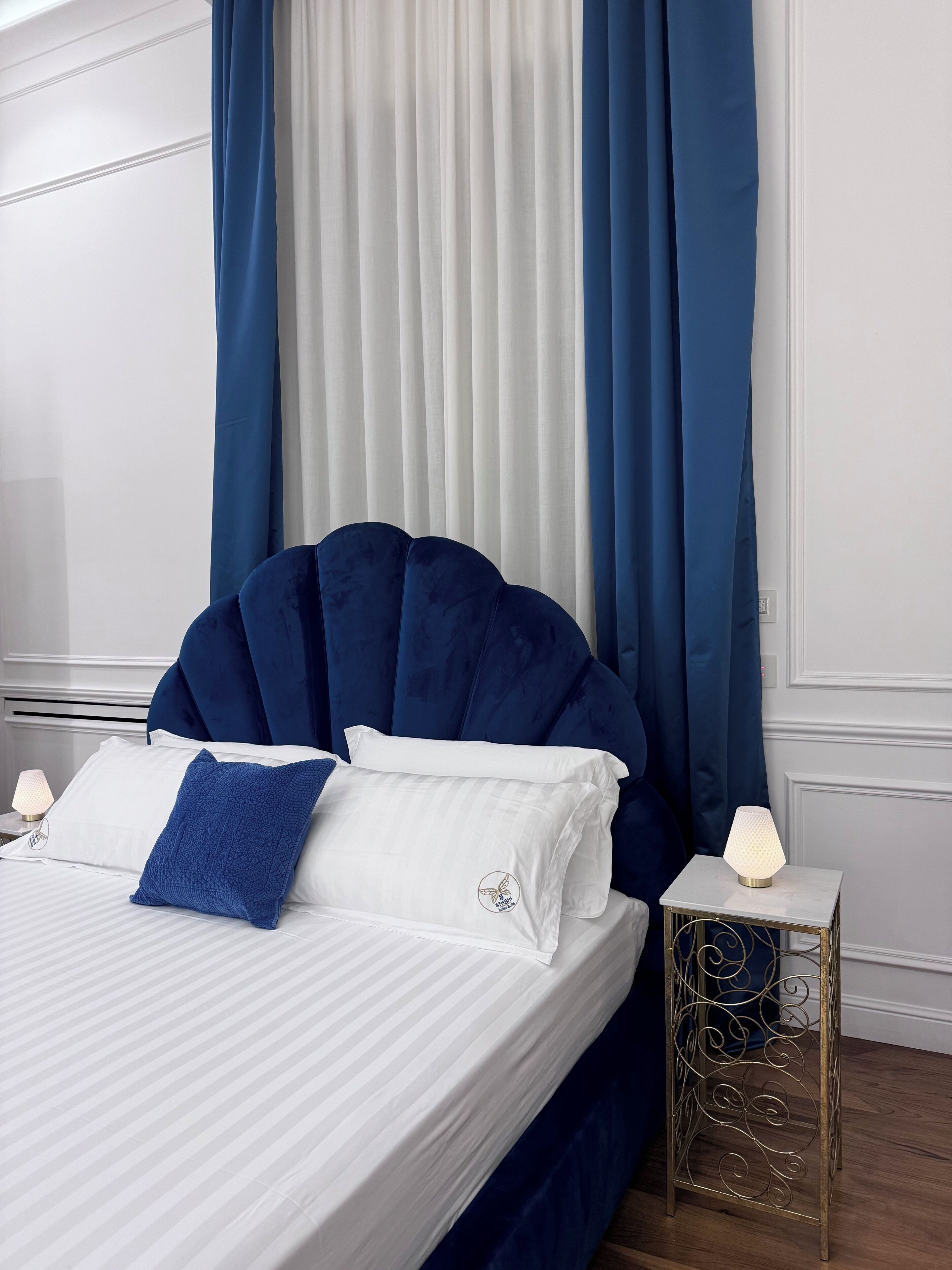 Uma cama bem arrumada com roupa de cama branca e azul, um cabeceiro azul e uma mesa de cabeceira com abajur.