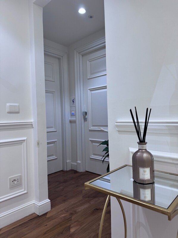 Un couloir aux murs blancs, doté d’un plancher en bois et d’une table en verre sur laquelle se trouve un diffuseur de parfum à bâtonnets.