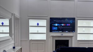Ein modernes Wohnzimmer mit Flachbildfernseher über einem Kamin, einem blauen Sofa und Holzboden.