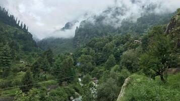 A mountainous landscape with a river, dense greenery, and a few buildings in the distance.
