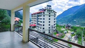 A balcony with a view of a multi-story building and a mountainous landscape. - Arigato Cottage (Manali)