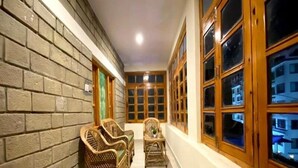 A corridor with brick walls, wicker furniture, and large windows with wooden frames. - Arigato Cottage (Manali)