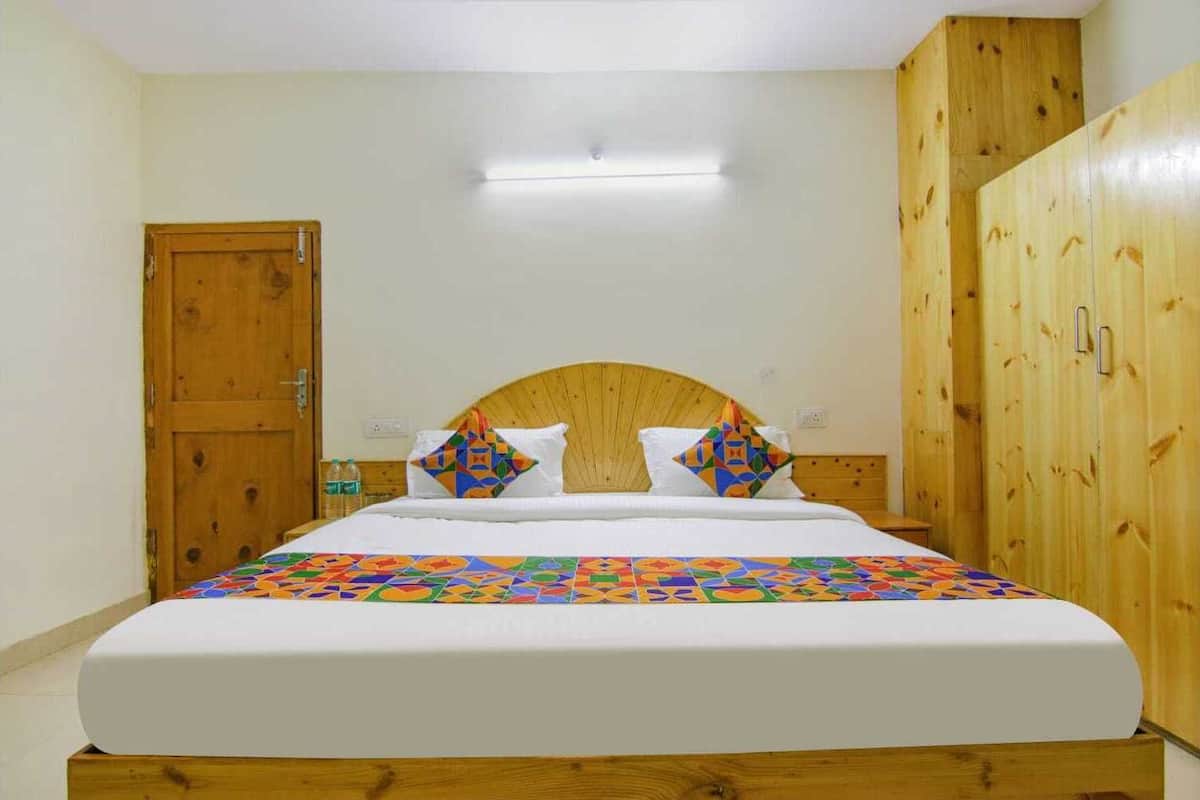 Un lit simple avec une tête de lit en bois, deux oreillers à motifs géométriques, un couvre-lit blanc et une armoire en bois sur le côté droit.