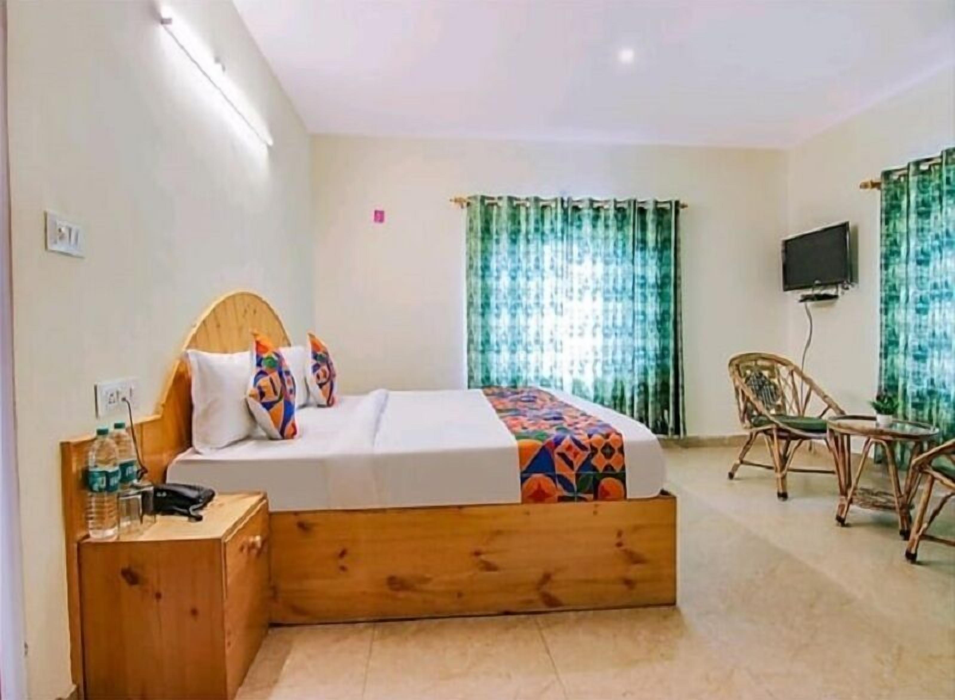 Een hotelkamer met een bed, een bureau, een stoel, een televisie en een raam met gordijnen.
