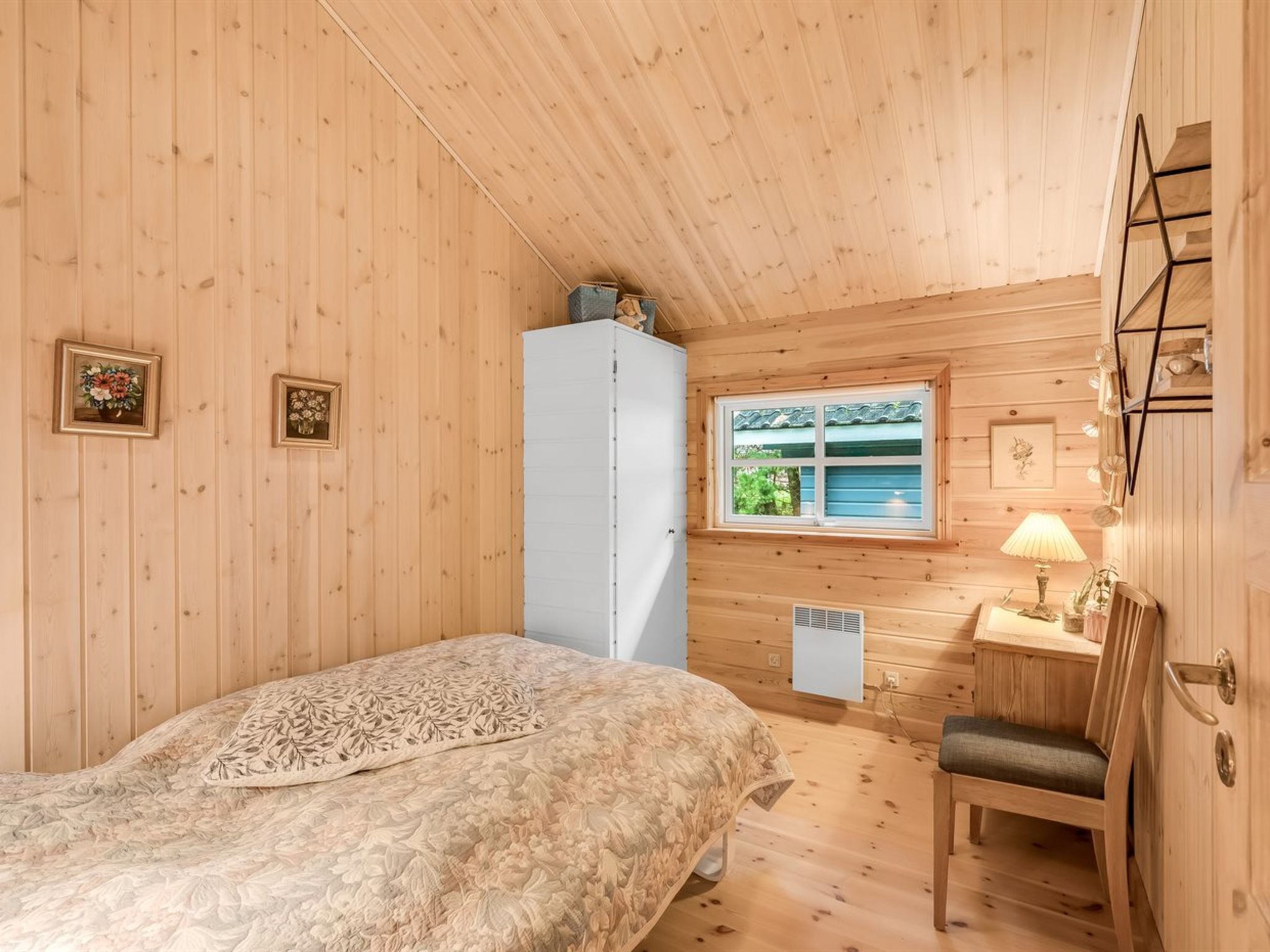 Une chambre confortable, aménagée dans un chalet en bois, avec un lit, un bureau, une chaise, une fenêtre et une armoire blanche.