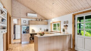 A modern kitchen with wooden cabinets, a central island, and a large window providing a view of greenery. - "Femme" by Interhome (Blåvand)