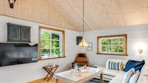 A cozy cabin interior with a wooden ceiling, a sofa, a table, and a TV. - "Femme" by Interhome (Blåvand)