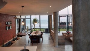 Un comedor espacioso con vistas al océano, que presenta una pared de ladrillo, iluminación moderna y un ventanal grande.