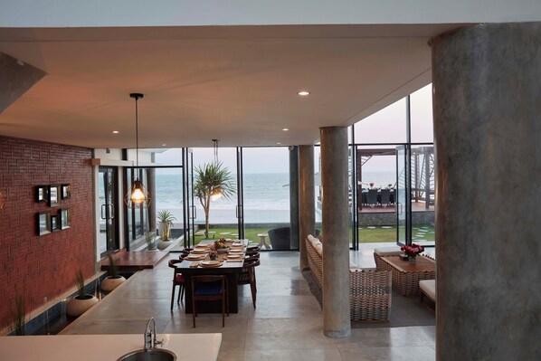 A spacious dining area with a view of the ocean, featuring a brick wall, modern lighting, and a large window. - Abian Kapas Beach Bali (Selemadeg)