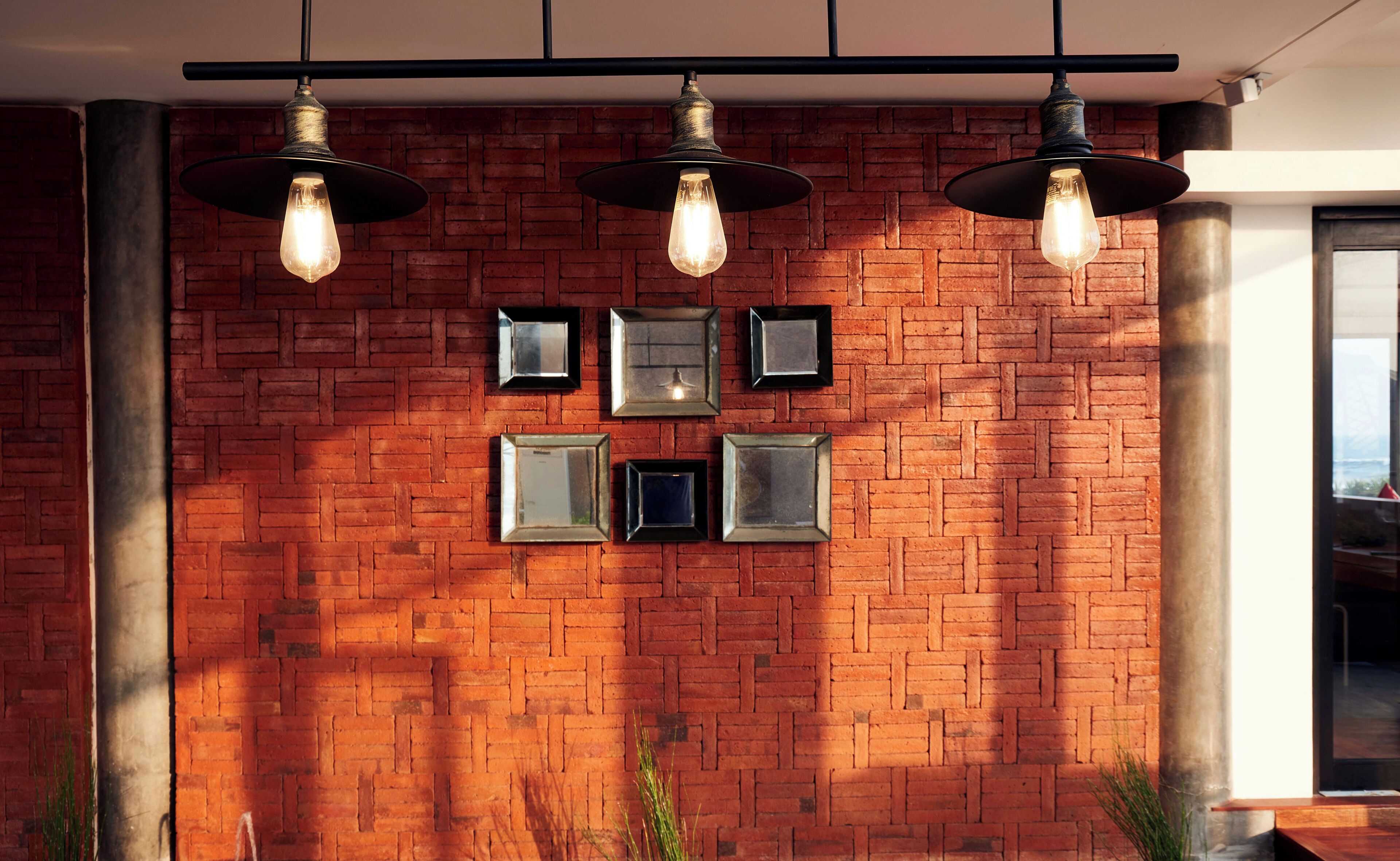 A brick wall with framed pictures and hanging pendant lights.