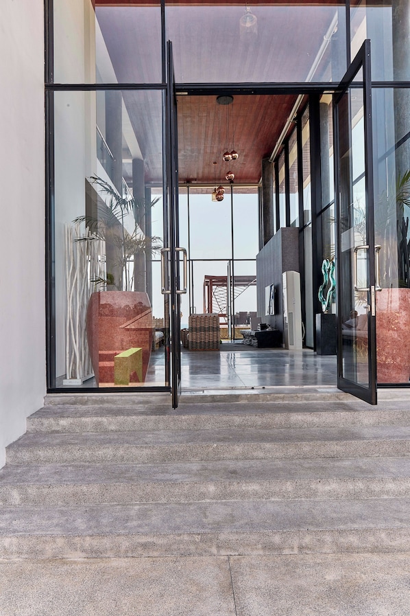 Una entrada moderna de edificio con puertas de cristal, techo de madera y vista al interior.