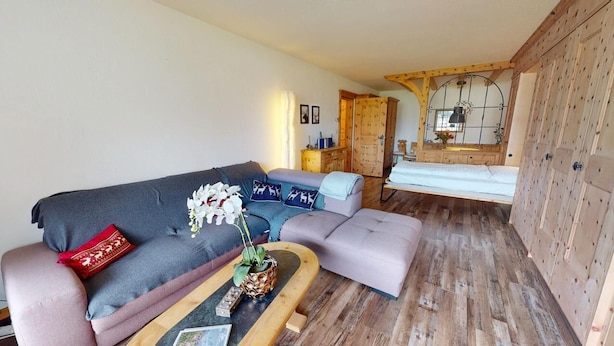 A cozy living room with a sofa, ottoman, and a wooden coffee table. There is a wooden wardrobe and a mirror on the wall. - Well-kept holiday apartament house in a prime location in St. (St. Moritz)