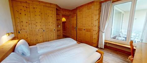 A wooden bedroom with a large bed, wooden wardrobe, and a window with curtains.