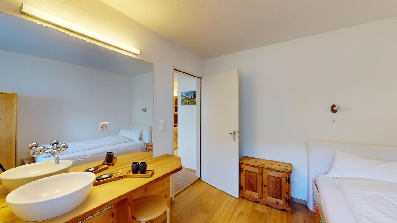 A bedroom with a bed, a wooden cabinet, a bedside table, and a large mirror.