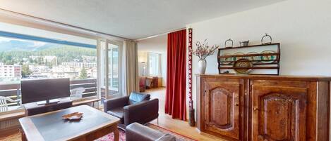 Ein geräumiges Wohnzimmer mit großem Fenster, einem Holzschrank und einem Fernseher.