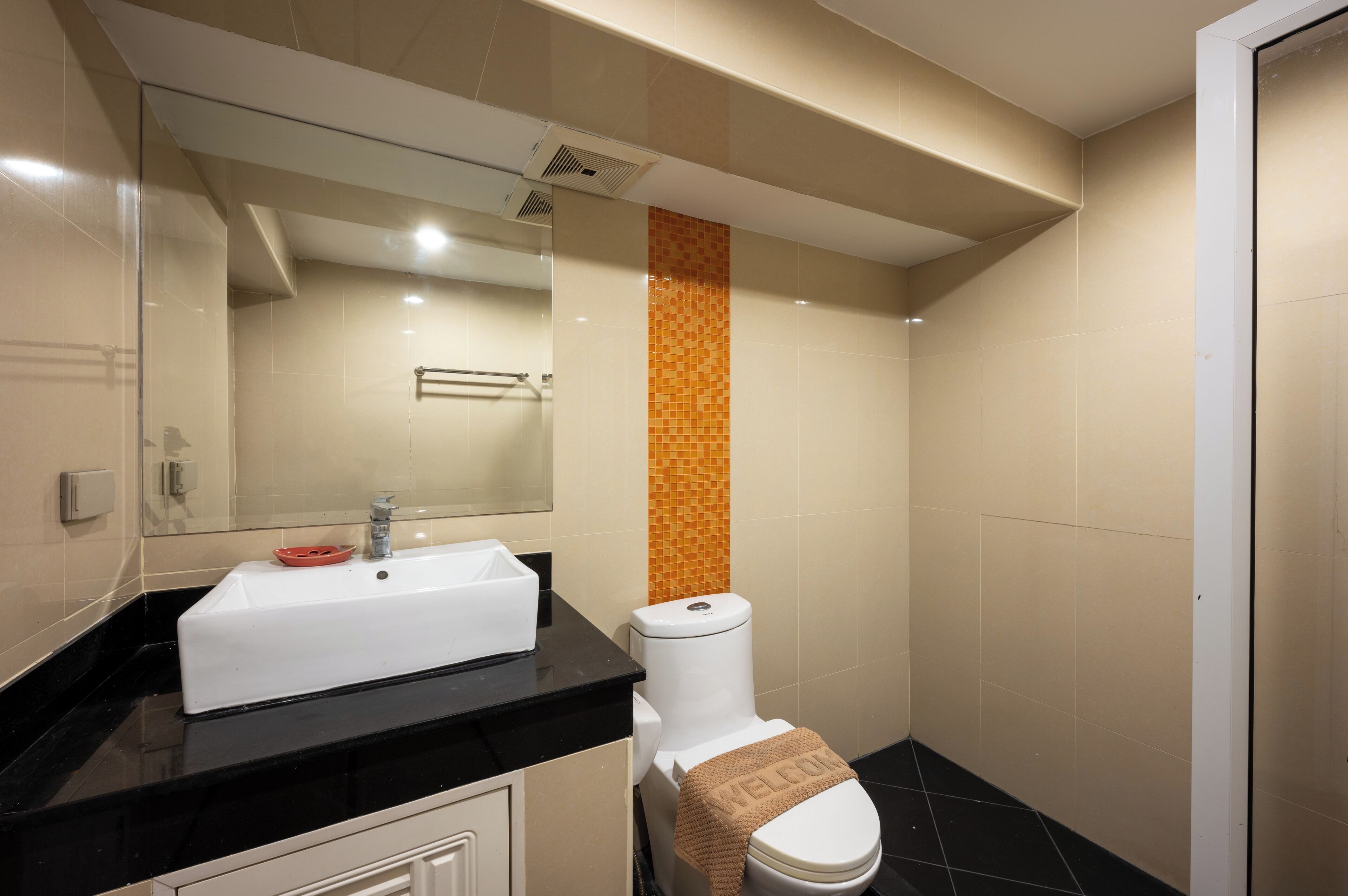 A bathroom with a white sink, black countertop, and a toilet with a towel on it.