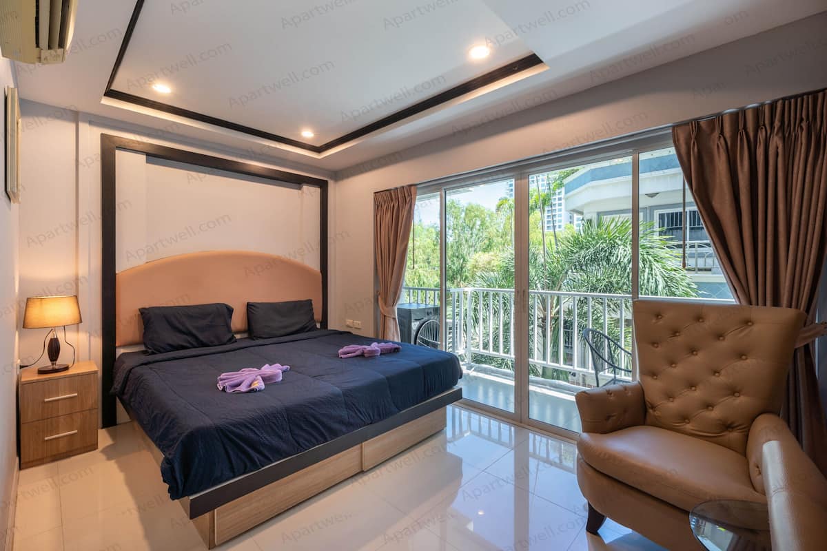 A bedroom with a bed, nightstand, lamp, and a view of a balcony.