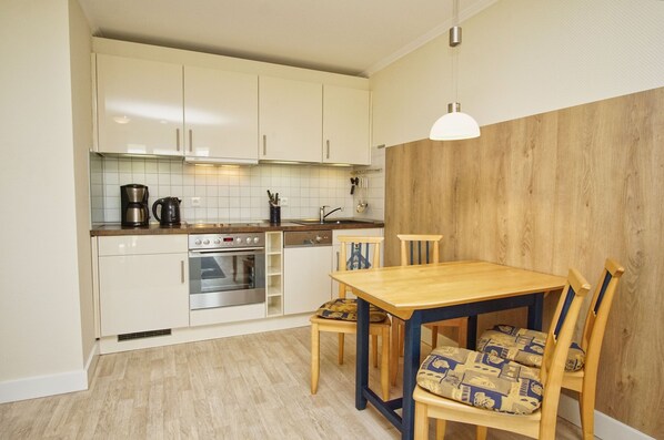 Cozinha compacta com armários brancos, mesa de jantar de madeira e luminária pendente.