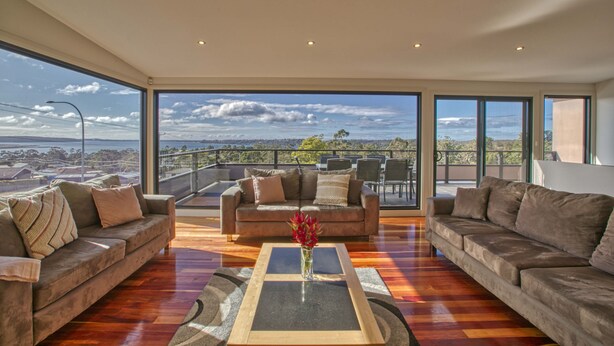 A spacious living room with a large window offering a view of the cityscape. - Georges Bay Luxury - St Helens (Break O'Day)