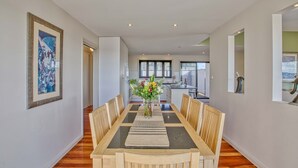 A dining area with a long table, chairs, and a vase of flowers. - Georges Bay Luxury - St Helens (Break O'Day)