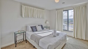 A bedroom with a large bed, a nightstand, a glass table, and a view through a window. - Georges Bay Luxury - St Helens (Break O'Day)