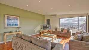 A spacious living room with a large window, a flat-screen TV, and a comfortable seating area. - Georges Bay Luxury - St Helens (Break O'Day)