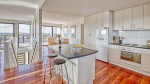 A modern kitchen with a central island, bar stools, a refrigerator, and an oven. - Georges Bay Luxury - St Helens (Break O'Day)