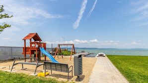 A playground with a slide, swings, and benches near a waterfront. - Lakefront Elegant Condo Lela (Balatonlelle)
