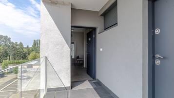 Fachada de un edificio moderno con una puerta azul oscuro, un balcón de cristal y un estacionamiento visible a través de las ventanas.