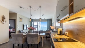 A modern kitchen with a wooden countertop, a dining area with chairs, and a view of the sea. - Lakefront Elegant Condo Lela (Balatonlelle)